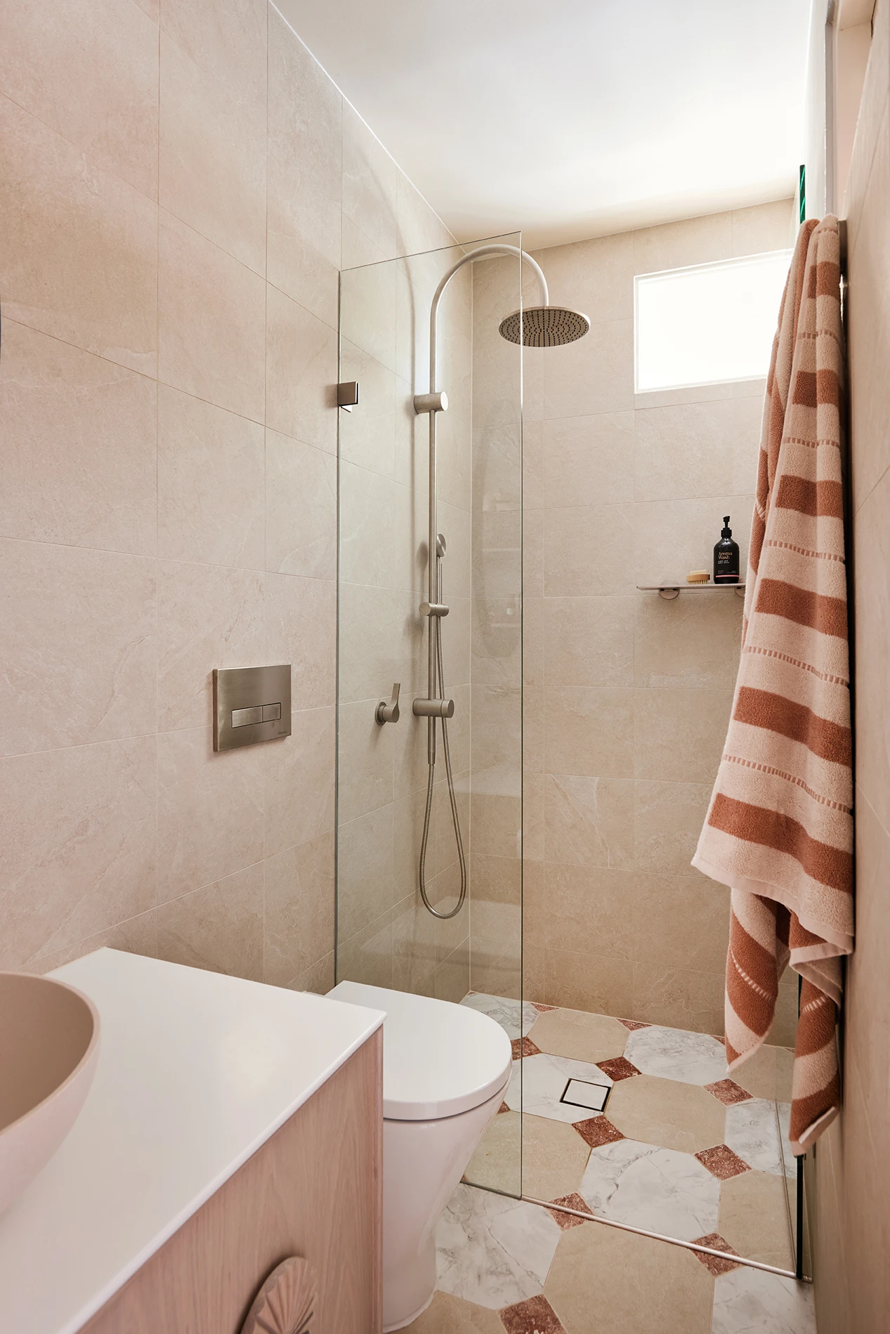 Bathroom with beige tiles, glass shower, rain showerhead, patterned floor tiles, toilet, vanity, and a striped towel hanging on the wall.