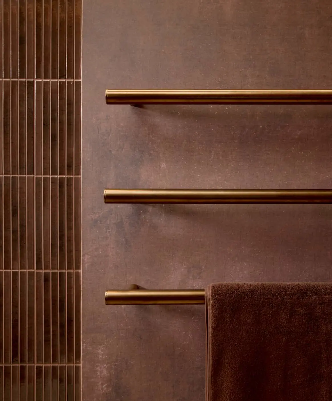 Modern bathroom with bronze towel rails mounted on textured walls, featuring brown towels and vertical tile.
