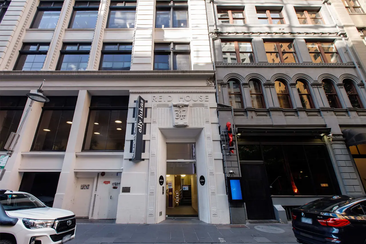 Historic city buildings with Elly Lukas Beauty Therapy College entrance in the center, featuring white and gray facades and parked cars below.