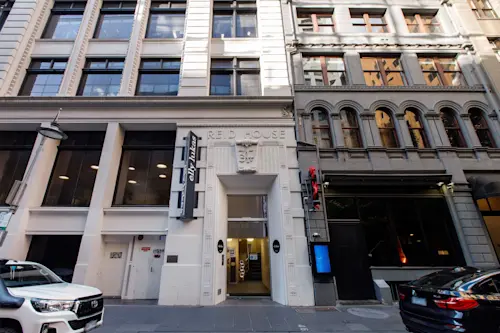 Historic city buildings with Elly Lukas Beauty Therapy College entrance in the center, featuring white and gray facades and parked cars below.