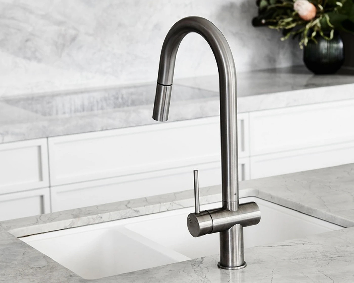 Modern stainless steel kitchen faucet with pull-down sprayer on marble countertop with white sink and small plant in background.