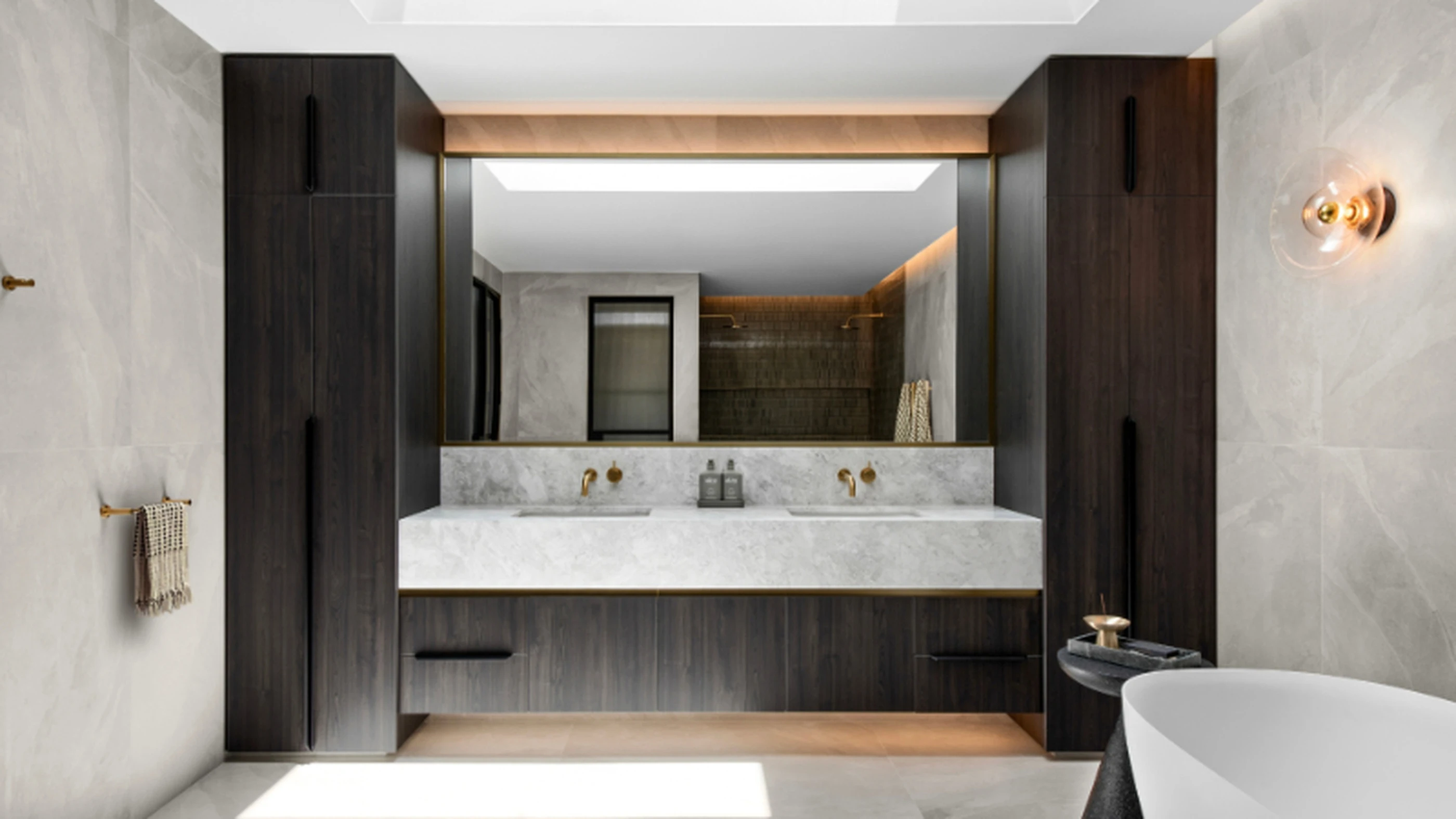 Modern bathroom with marble countertop, dark wood cabinetry, gold fixtures, and a large mirror with ambient lighting.