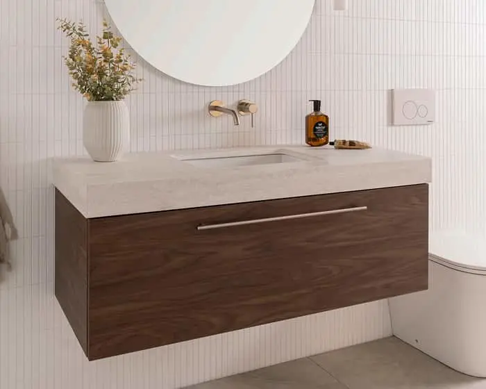 Modern bathroom vanity with wooden cabinet, stone countertop, wall-mounted faucet, and decorative plant against white tiled wall.