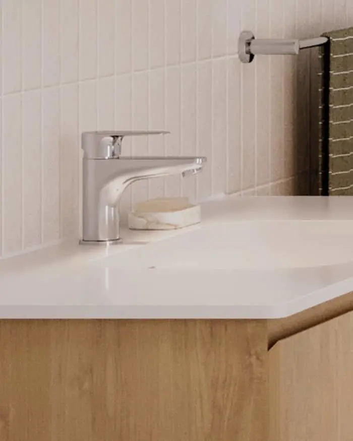 Modern bathroom sink with chrome faucet on white countertop, wooden cabinet base, and white tiled wall.