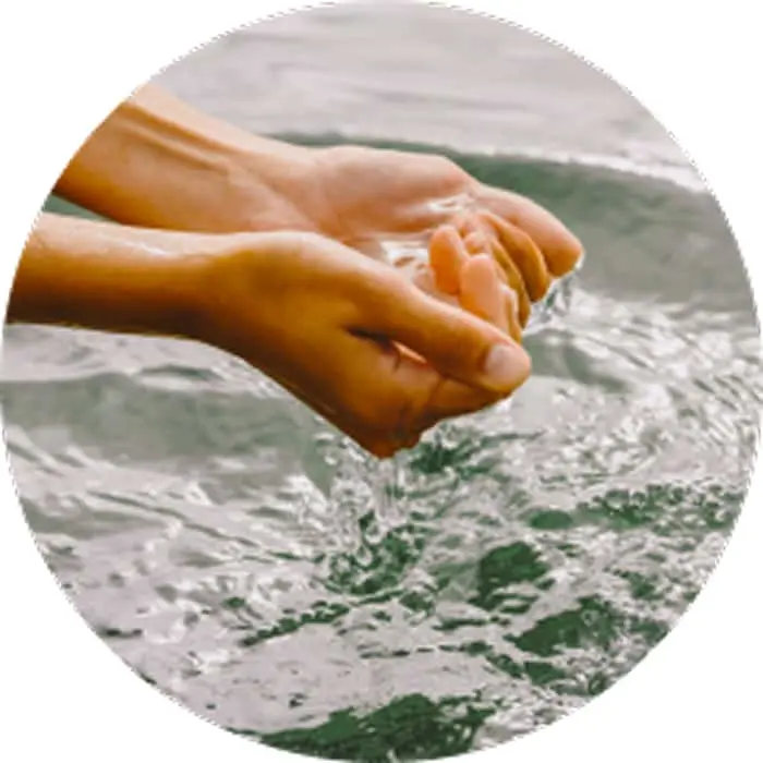 Hands gently touching clear water surface, creating ripples in a circular framed image.