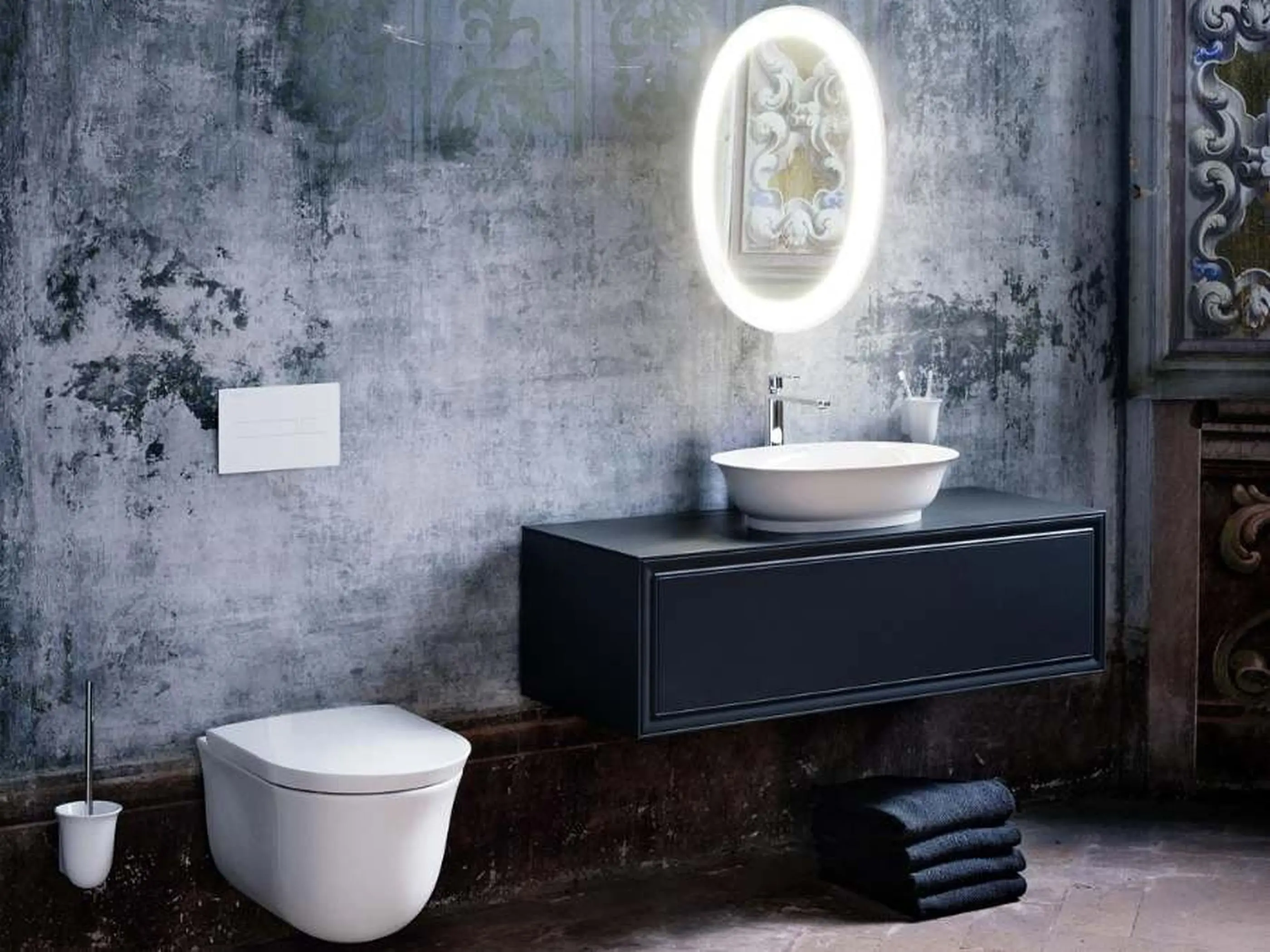 Modern bathroom with concrete walls, black vanity, white vessel sink, illuminated round mirror, and wall-mounted toilet.