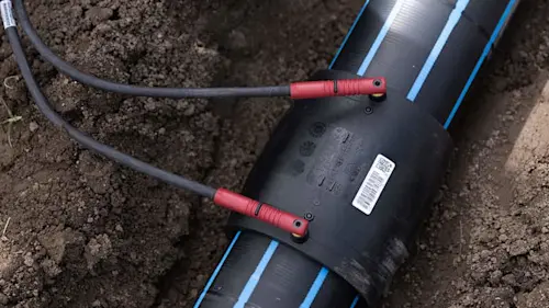 Black pipe with blue stripes connected to red-tipped cables, installed in soil for underground water system.