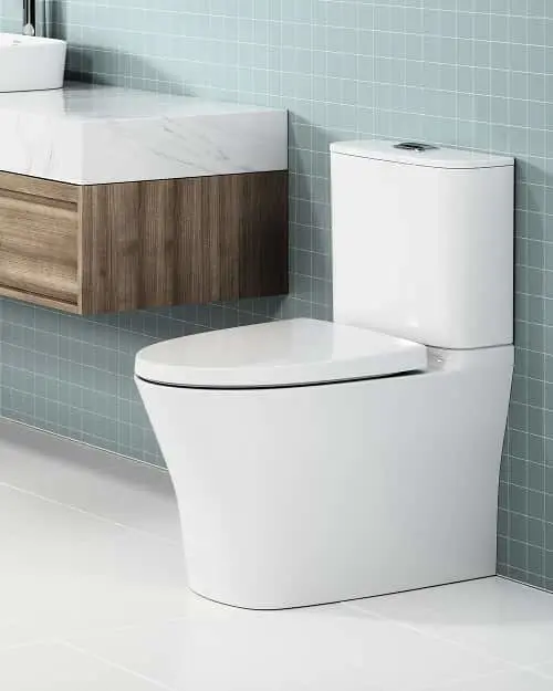 Modern bathroom with white toilet and floating wooden vanity with marble top against light blue tiled wall.