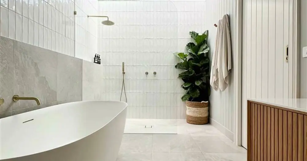 Modern white bathroom with freestanding tub, walk-in shower, potted plant, and beige towels on a minimalist design.