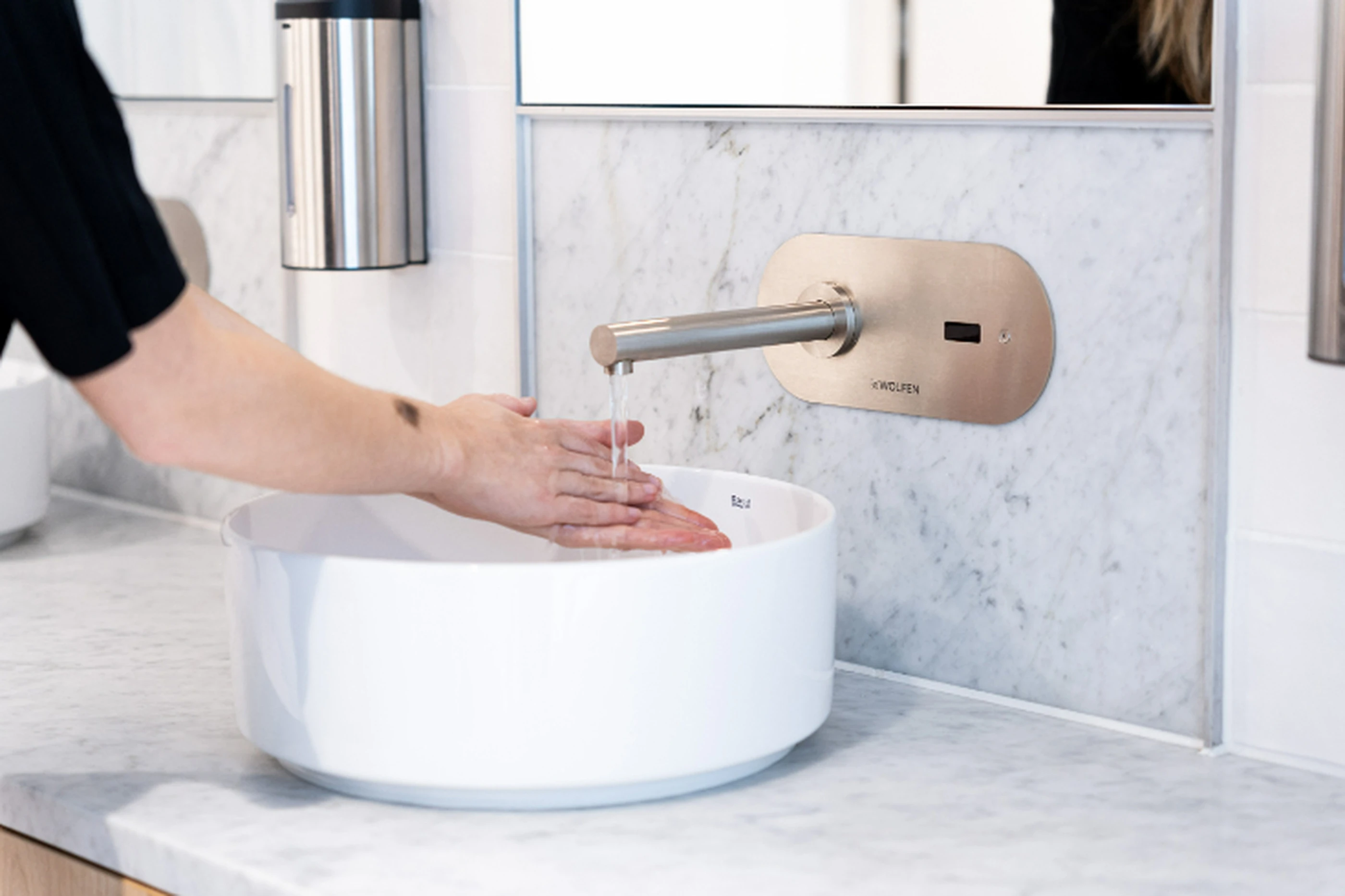Person washing hands in a white basin sink with modern wall-mounted faucet against marble bathroom wall.
