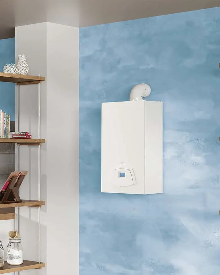 White wall-mounted boiler with exhaust pipe on light blue textured wall, wooden shelving unit visible to the left.