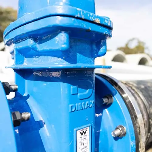 Close-up of a bright blue DIMAX water valve or pipe fitting with metal bolts and a white label visible.