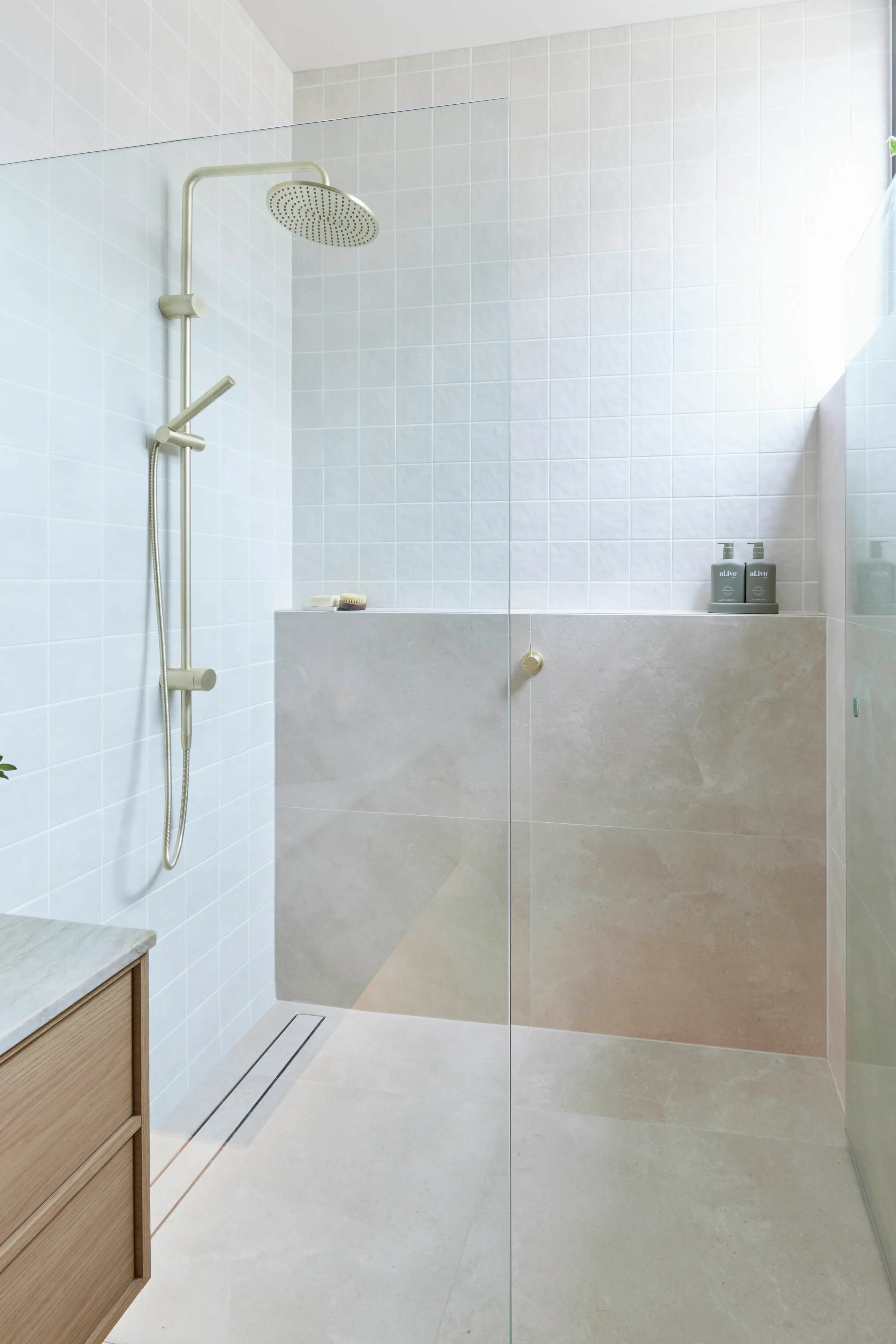 Modern walk-in shower with light blue tile walls, brushed gold fixtures, and built-in shelf for toiletries.