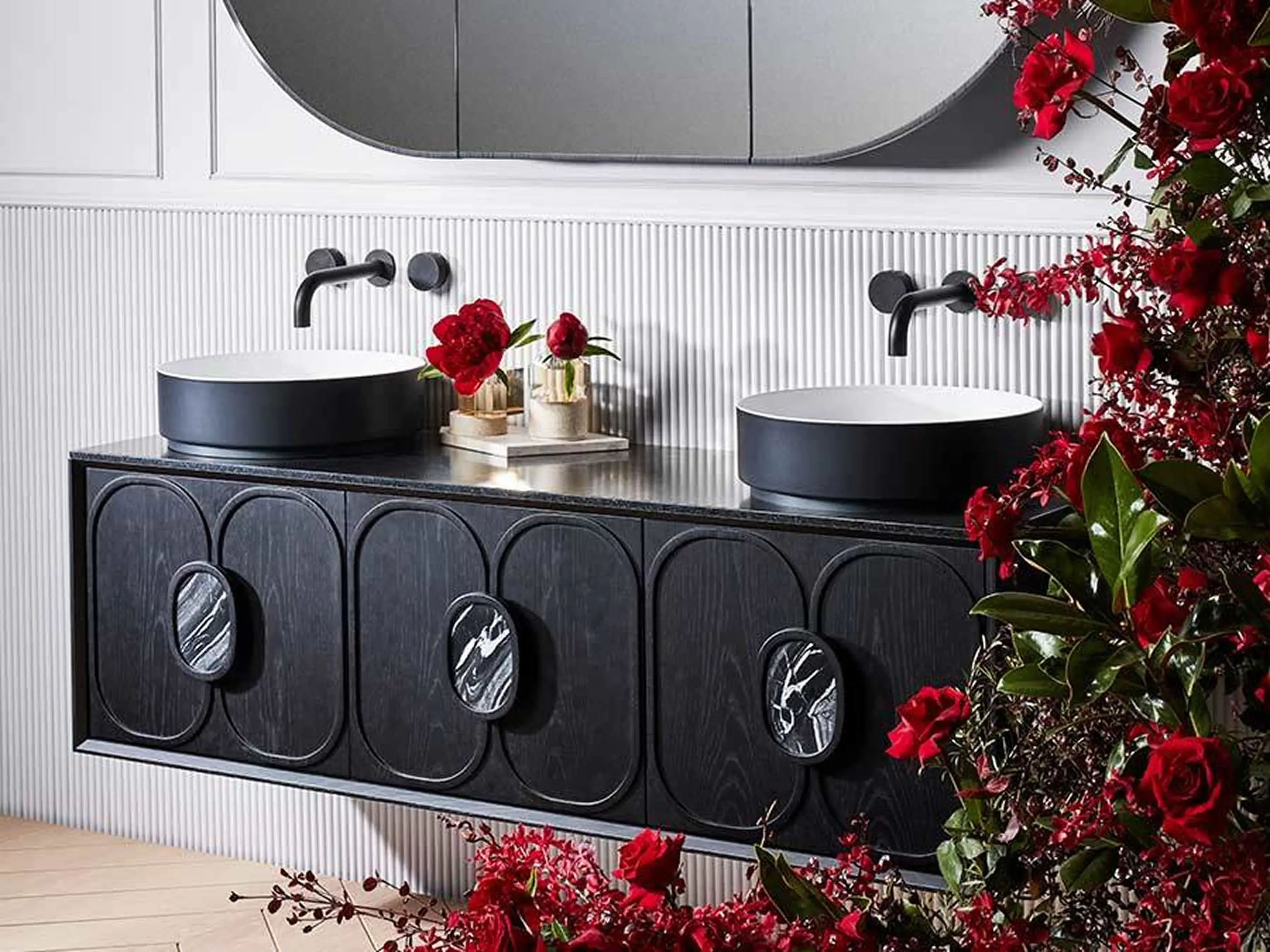 Modern black bathroom vanity with two vessel sinks, wall-mounted faucets, and vibrant red flowers decorating the space.