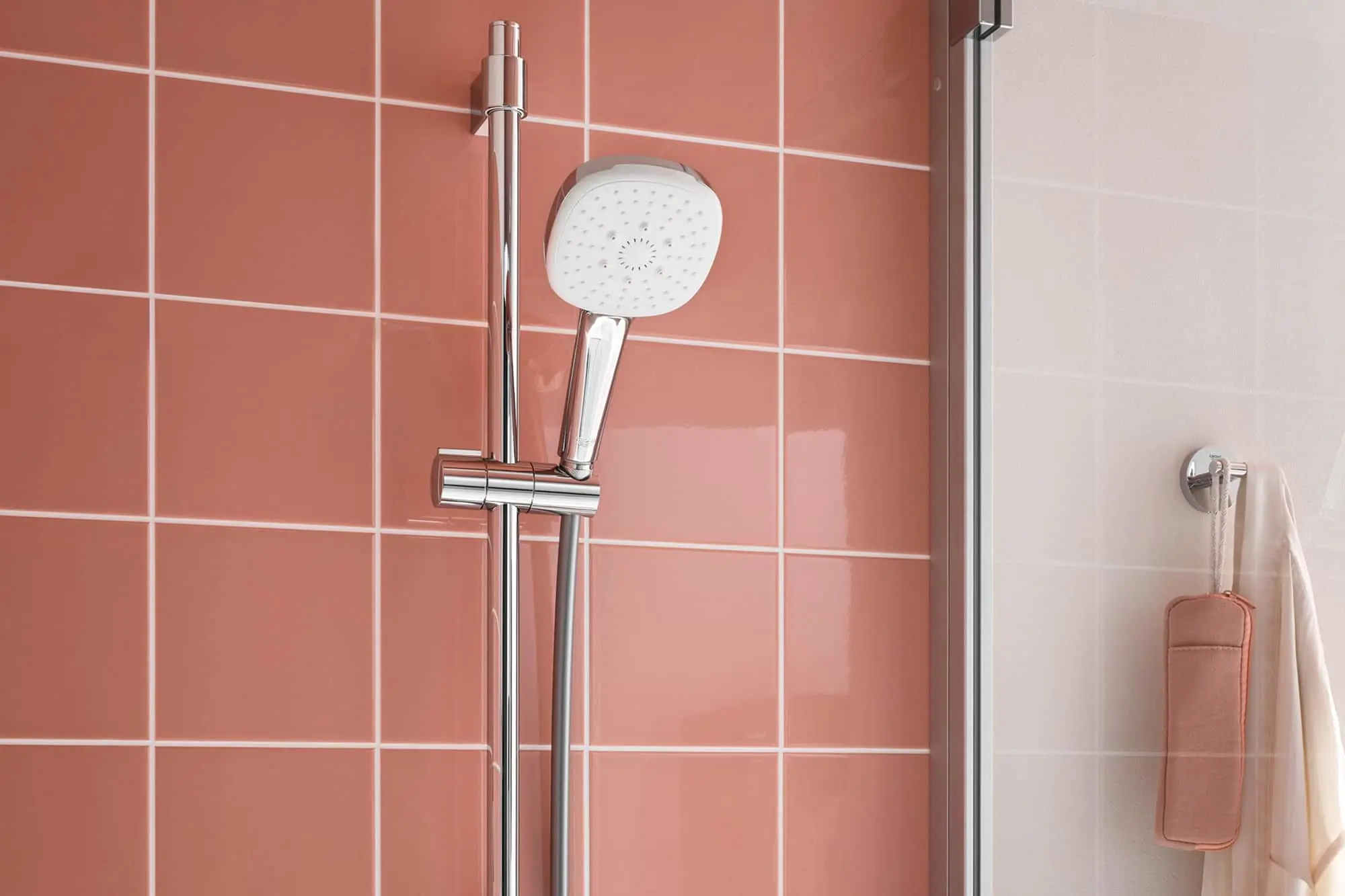 Modern shower head with adjustable rail mounted on coral pink tiled wall, with shower accessories hanging nearby.