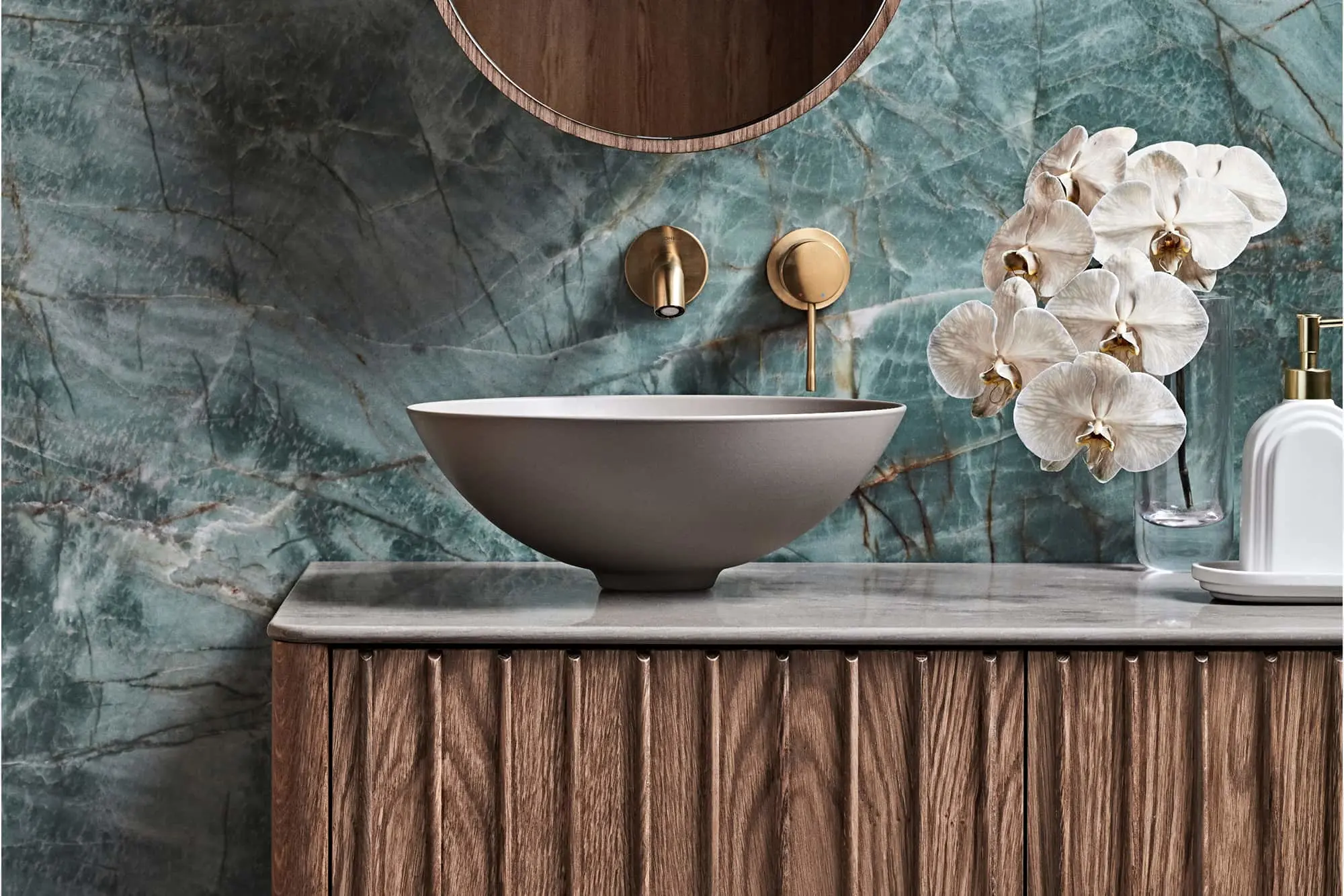 Luxury bathroom with green marble wall, vessel sink on wooden vanity, gold fixtures, and white orchids.