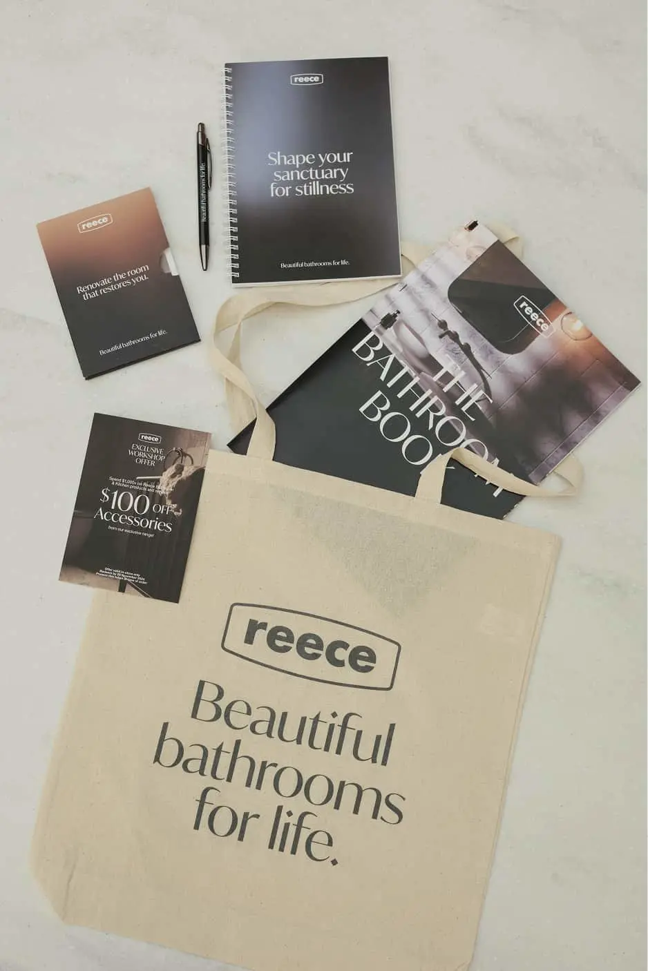 Reece bathroom marketing materials including a canvas tote bag, notebook, brochures, and promotional materials on marble surface.