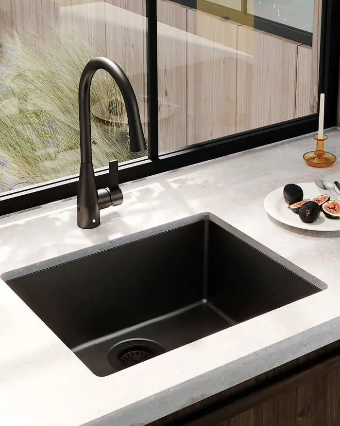 Modern black kitchen sink with matching faucet on white countertop, window view and plate with figs nearby.