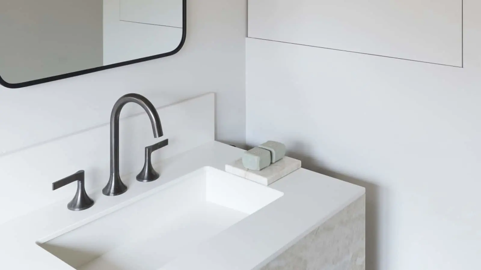 Modern bathroom sink with matte black faucet on white countertop, small soap dish, and partial mirror view.