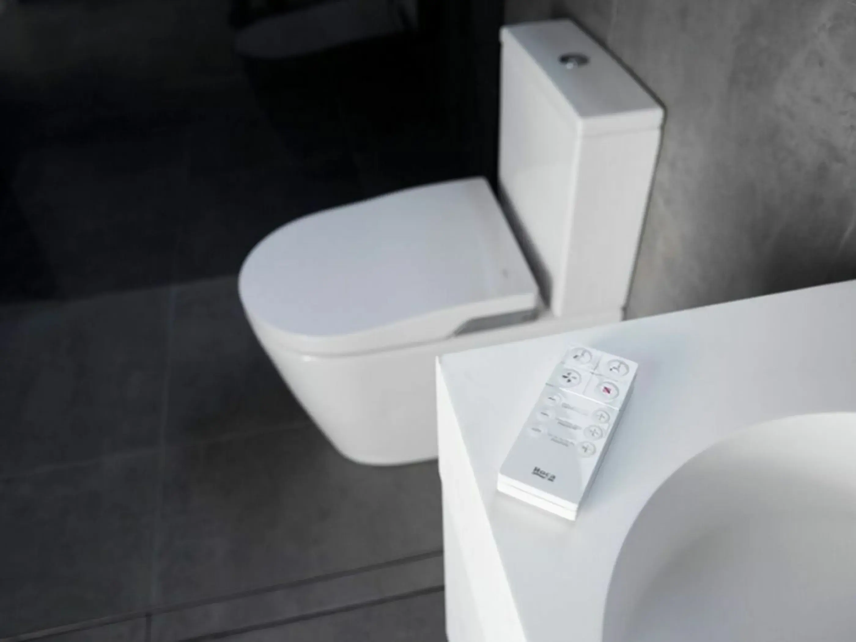 Modern white toilet with electronic remote control resting on the edge of the bathroom fixture.