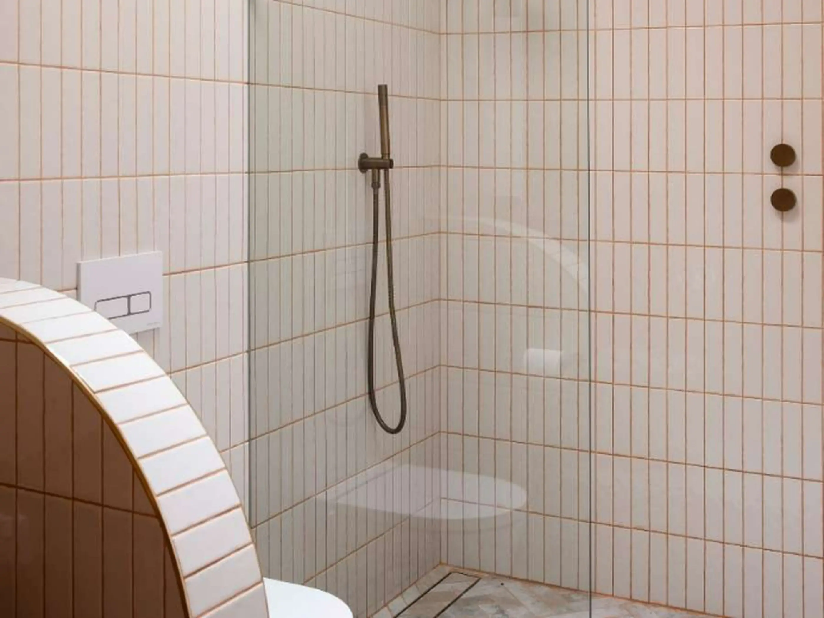 Modern shower stall with white vertical tiles, bronze fixtures, and glass partition in a minimalist bathroom design.