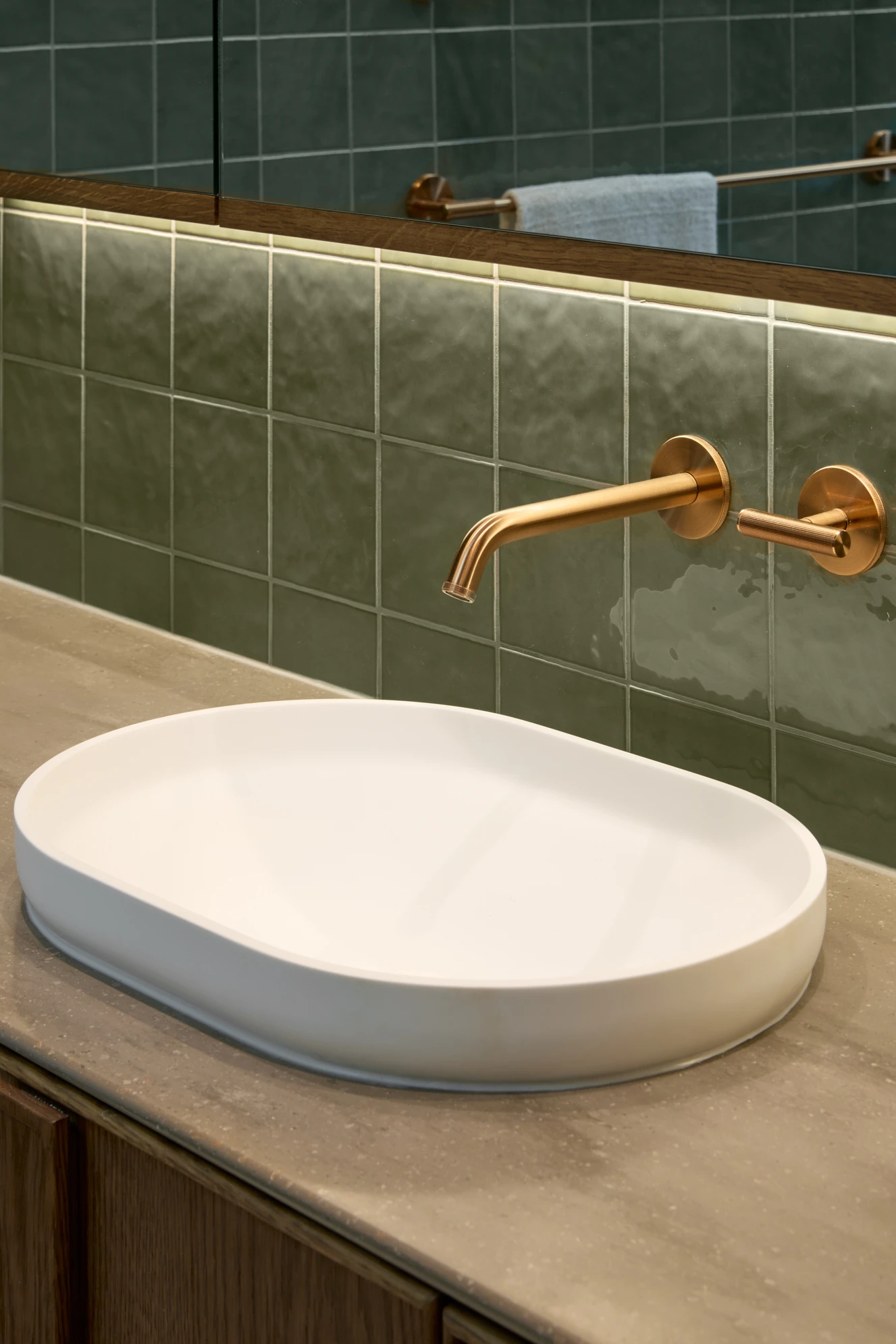 Modern bathroom with white oval vessel sink, brass wall-mounted faucet, and green tile backsplash with mirror above.