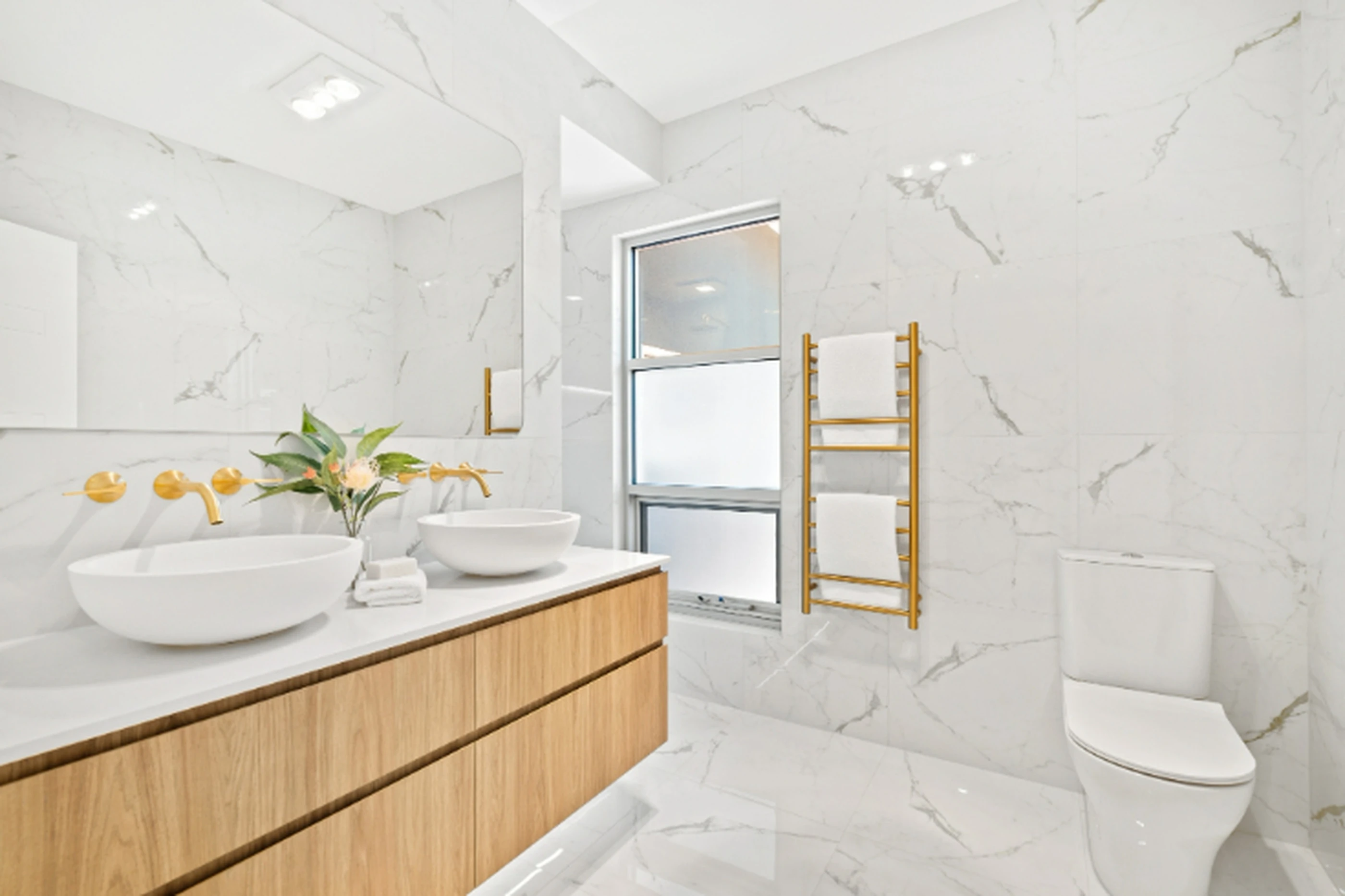 Modern bathroom with white marble tiles, wooden vanity with bowl sinks, gold fixtures, and a heated towel rack.