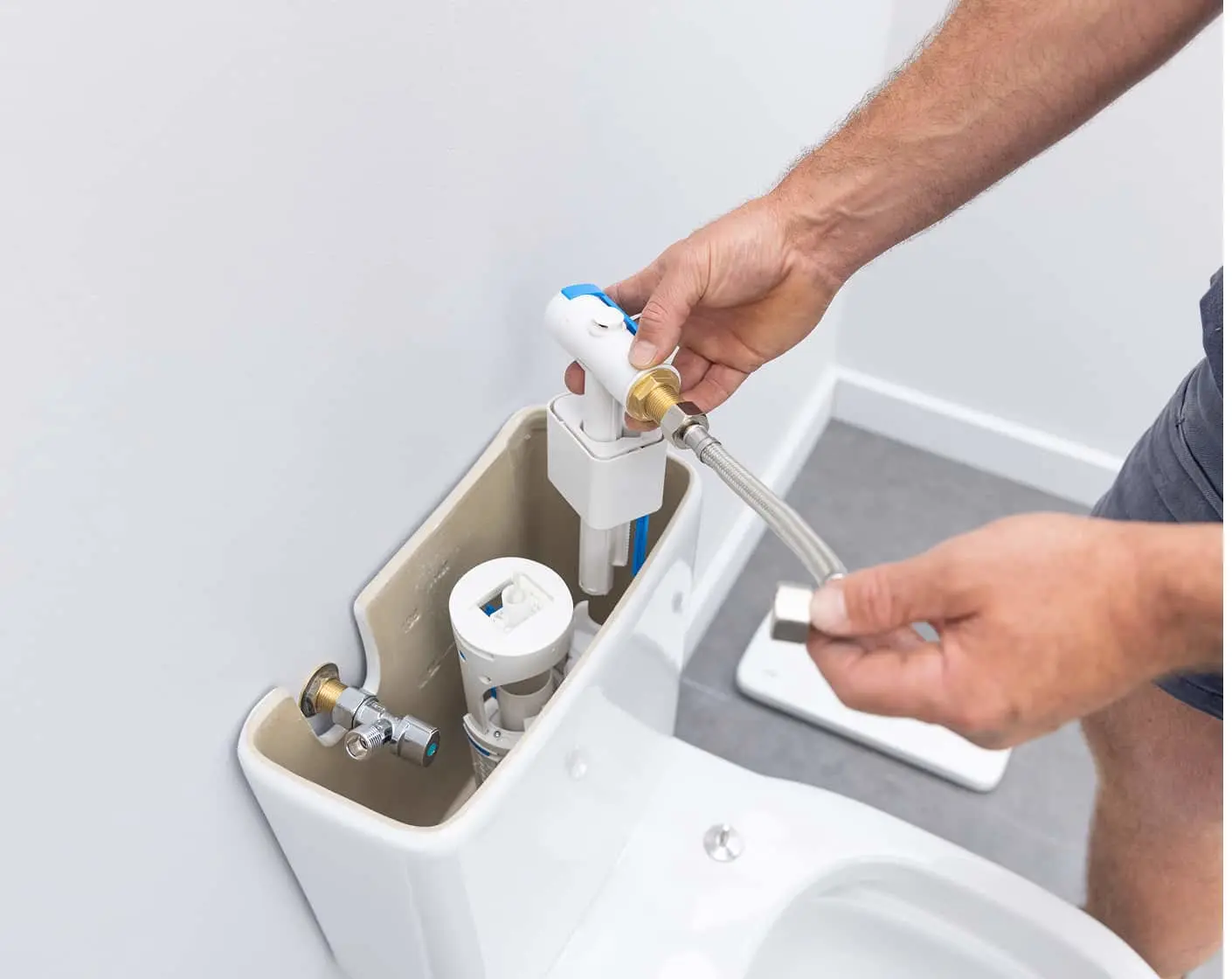 Person repairing toilet tank by connecting water supply hose to fill valve mechanism.