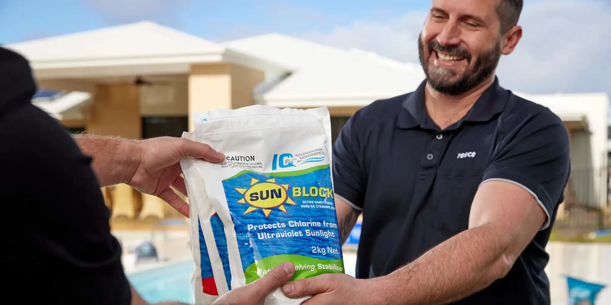 Person in navy polo shirt receiving a bag of Sun Block pool chlorine stabilizer, with swimming pool in background.