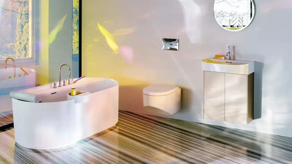 Modern bathroom with white freestanding tub, wall-mounted toilet, vanity sink, and round mirror on striped wooden floor.