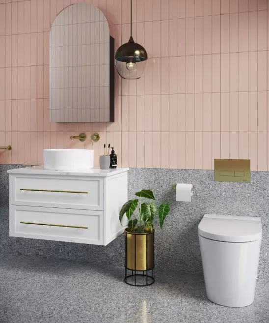 Modern bathroom with pink tile walls, arched mirror, white vanity, pendant light, and potted plant beside toilet.
