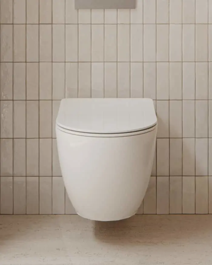 White wall-mounted toilet with closed lid against beige vertical tiled bathroom wall.