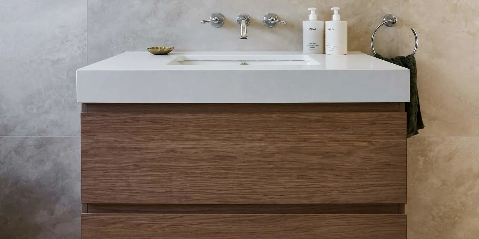 Modern bathroom vanity with white countertop, wooden cabinet, wall-mounted faucet, and two product bottles.