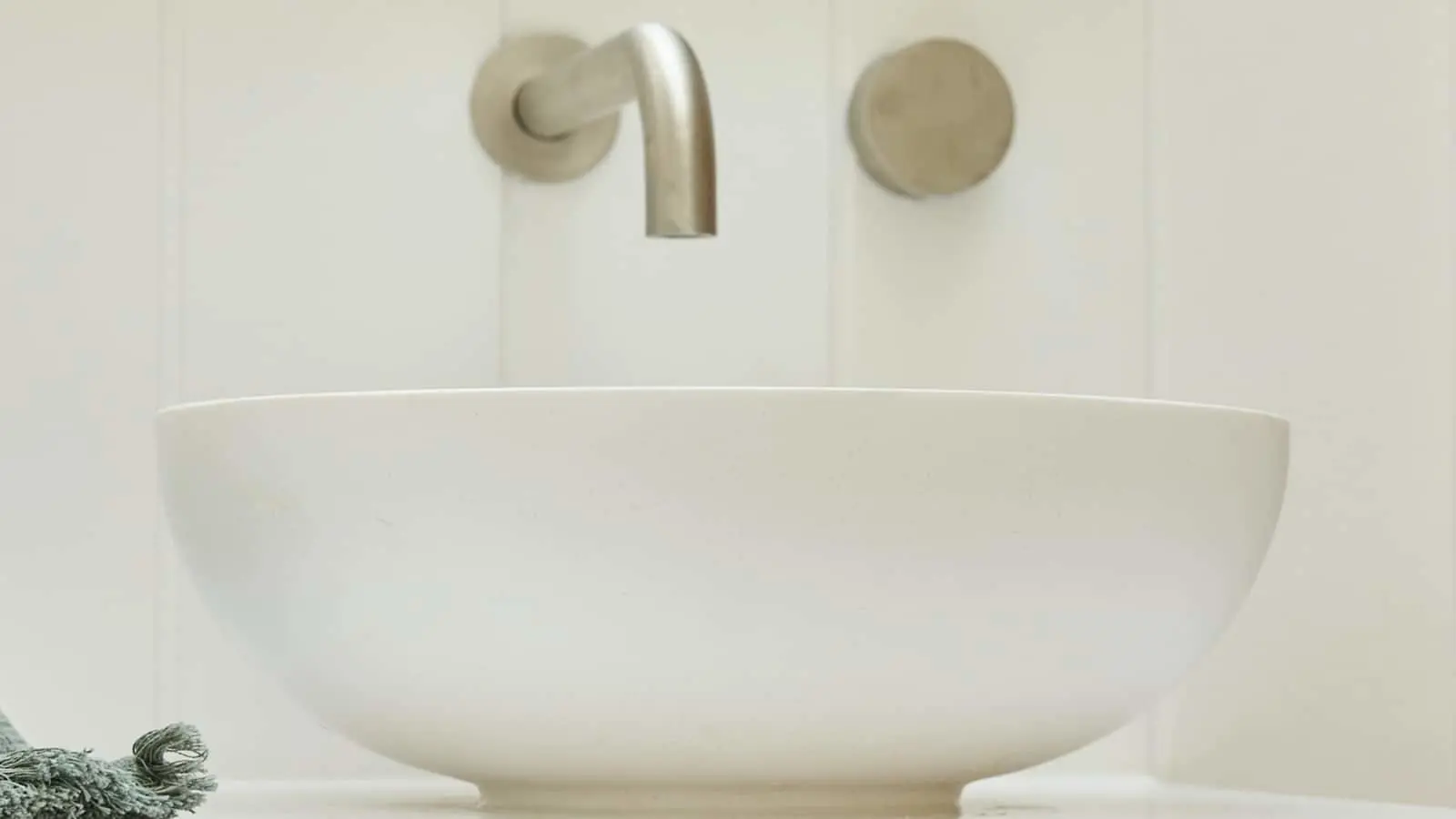 Modern white bowl sink with brushed nickel wall-mounted faucet against white tiled bathroom wall.