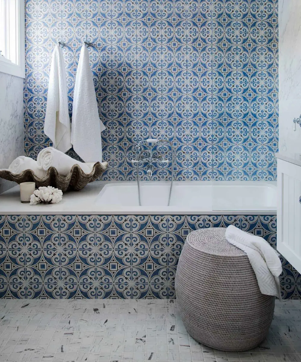 Bathroom with white bathtub, blue and white patterned tiles, shell decoration, rolled towels, and wicker basket.