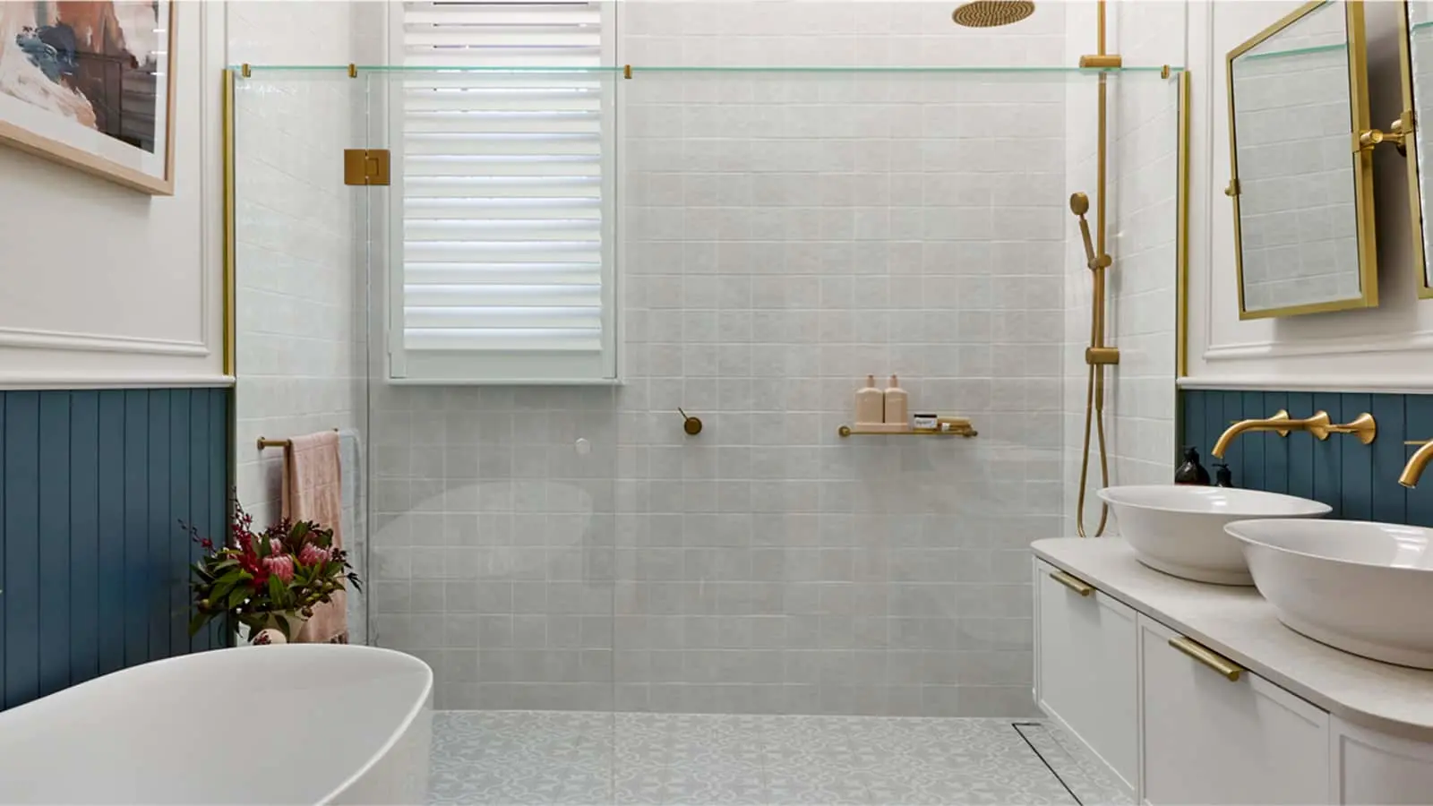 Modern bathroom with white tiles, blue wainscoting, glass shower, double vessel sinks, and gold fixtures.