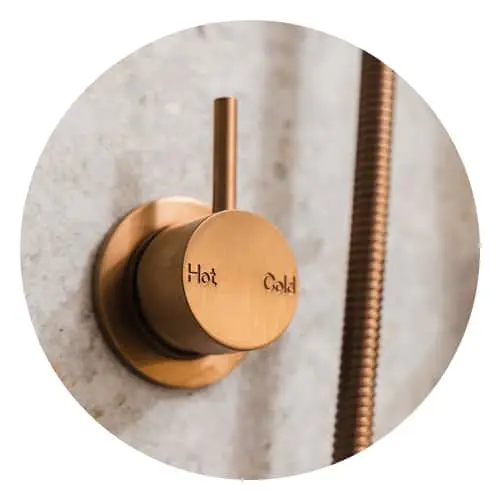 Brass shower control knob labeled "Hot Cold" mounted on a marble wall with copper piping visible.