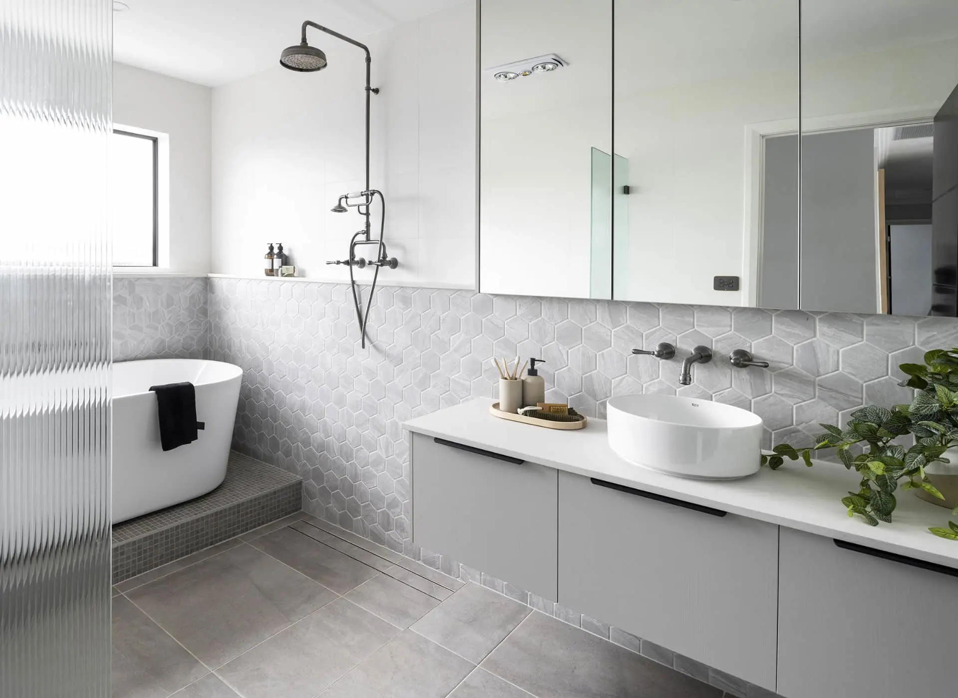 Modern white bathroom with hexagonal tile backsplash, freestanding tub, vessel sink, and black fixtures.