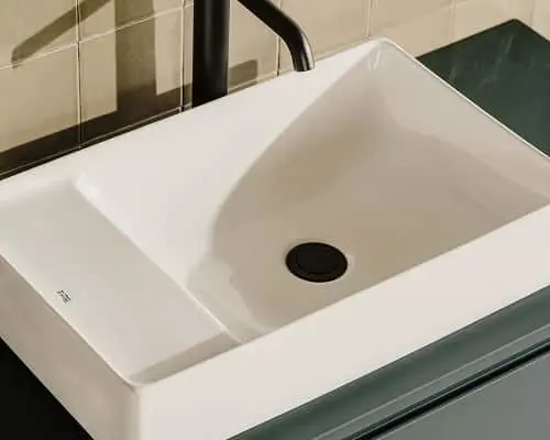 White rectangular bathroom sink with black drain and faucet on green vanity with beige tiled wall behind.