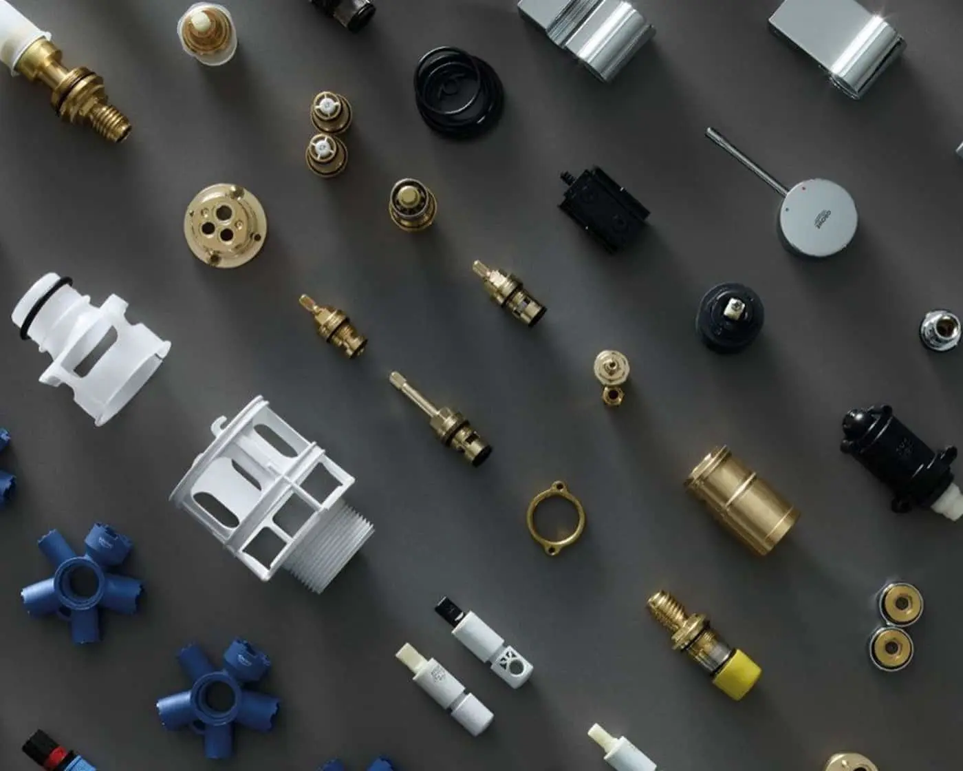 Various plumbing components and fittings arranged on a dark gray surface, including brass valves, plastic connectors, and metal parts.