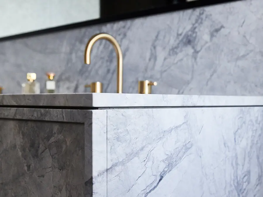 Elegant bathroom vanity with marble countertop and backsplash, featuring a gold faucet and small perfume bottles.