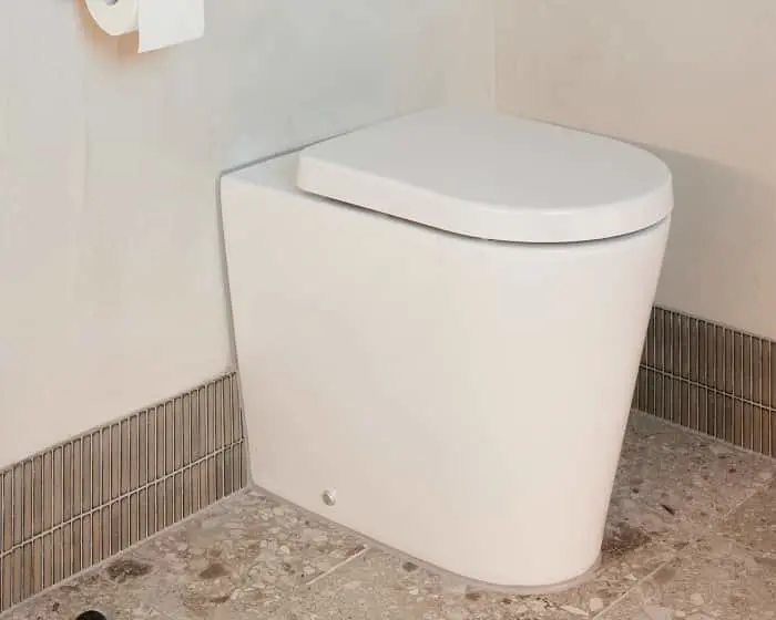 Modern white toilet with closed lid in a bathroom with beige tile border and stone-look floor tiles.
