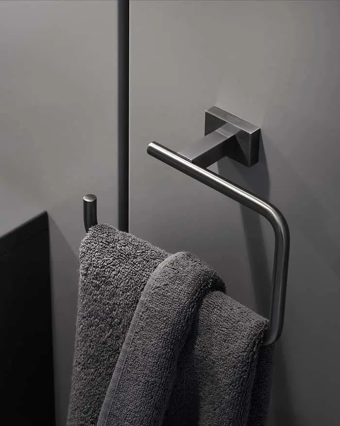 Modern stainless steel towel holder with gray towels hanging on it, mounted on a gray bathroom wall.