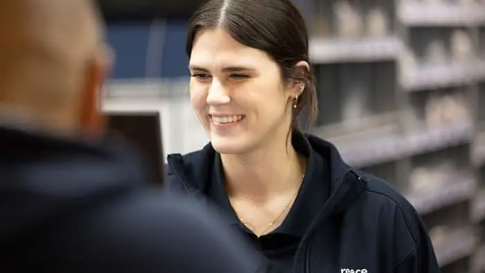 Person in navy blue uniform smiling during conversation in retail environment with blurred shelving in background.