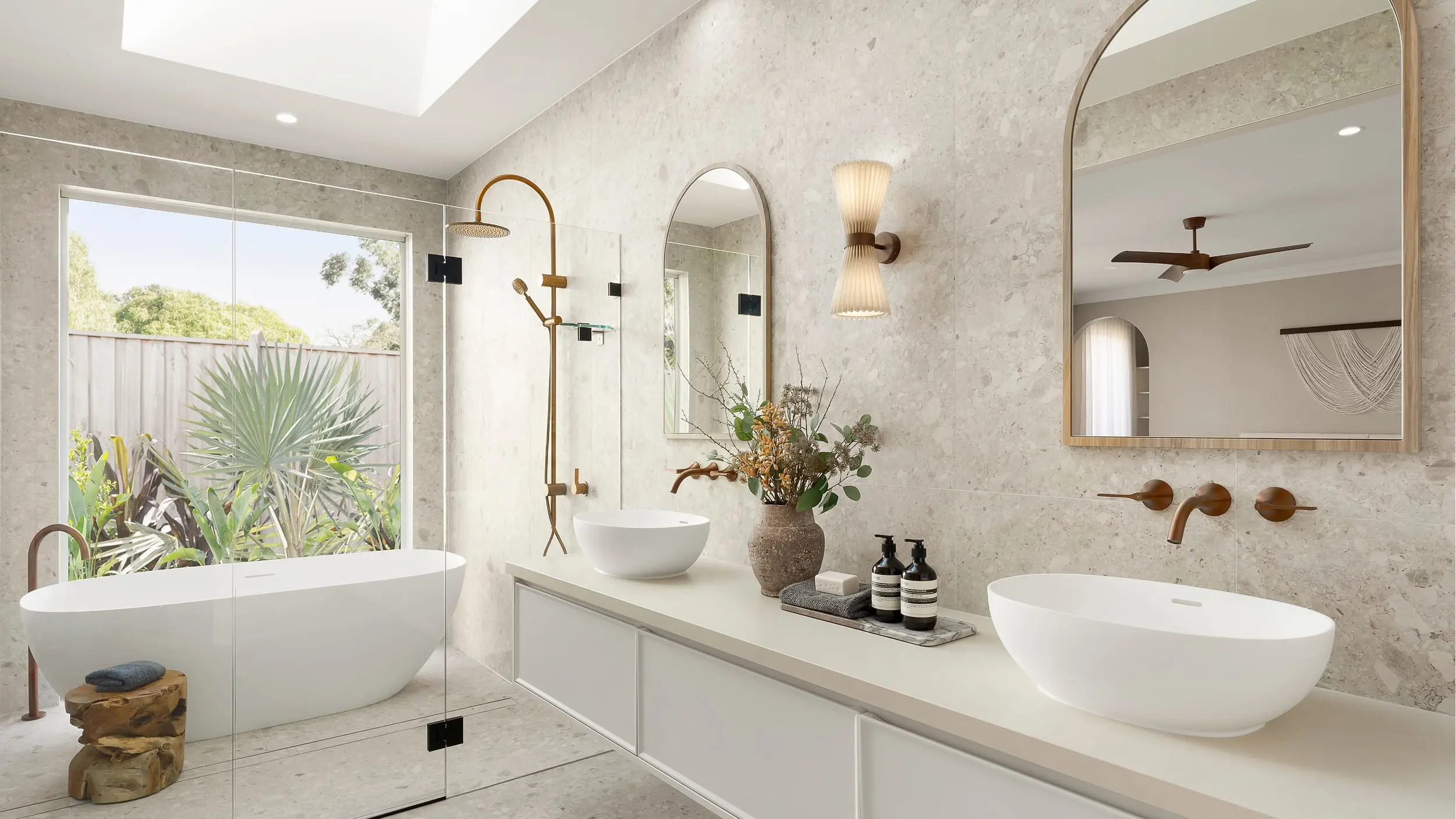 Modern luxury bathroom with marble walls, white freestanding tub, double vessel sinks, and large window overlooking plants.