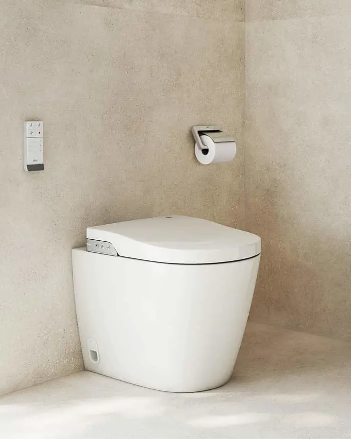 Modern white toilet with electronic control panel in a minimalist bathroom with beige walls and toilet paper holder.