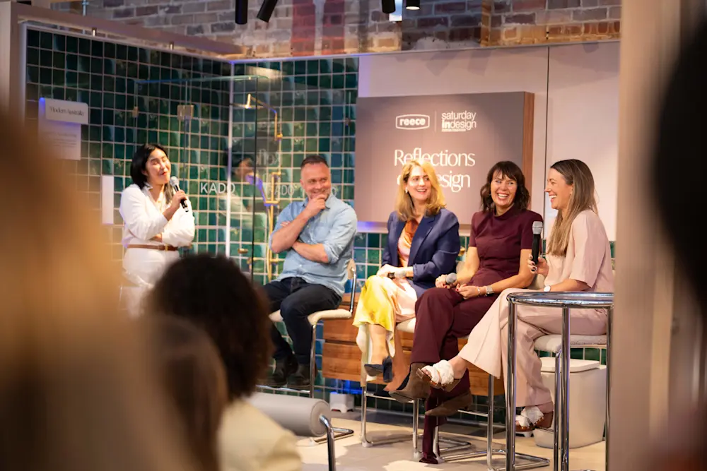 Five people on stage at a panel discussion with green tiled backdrop and Reflections in Design sign visible.