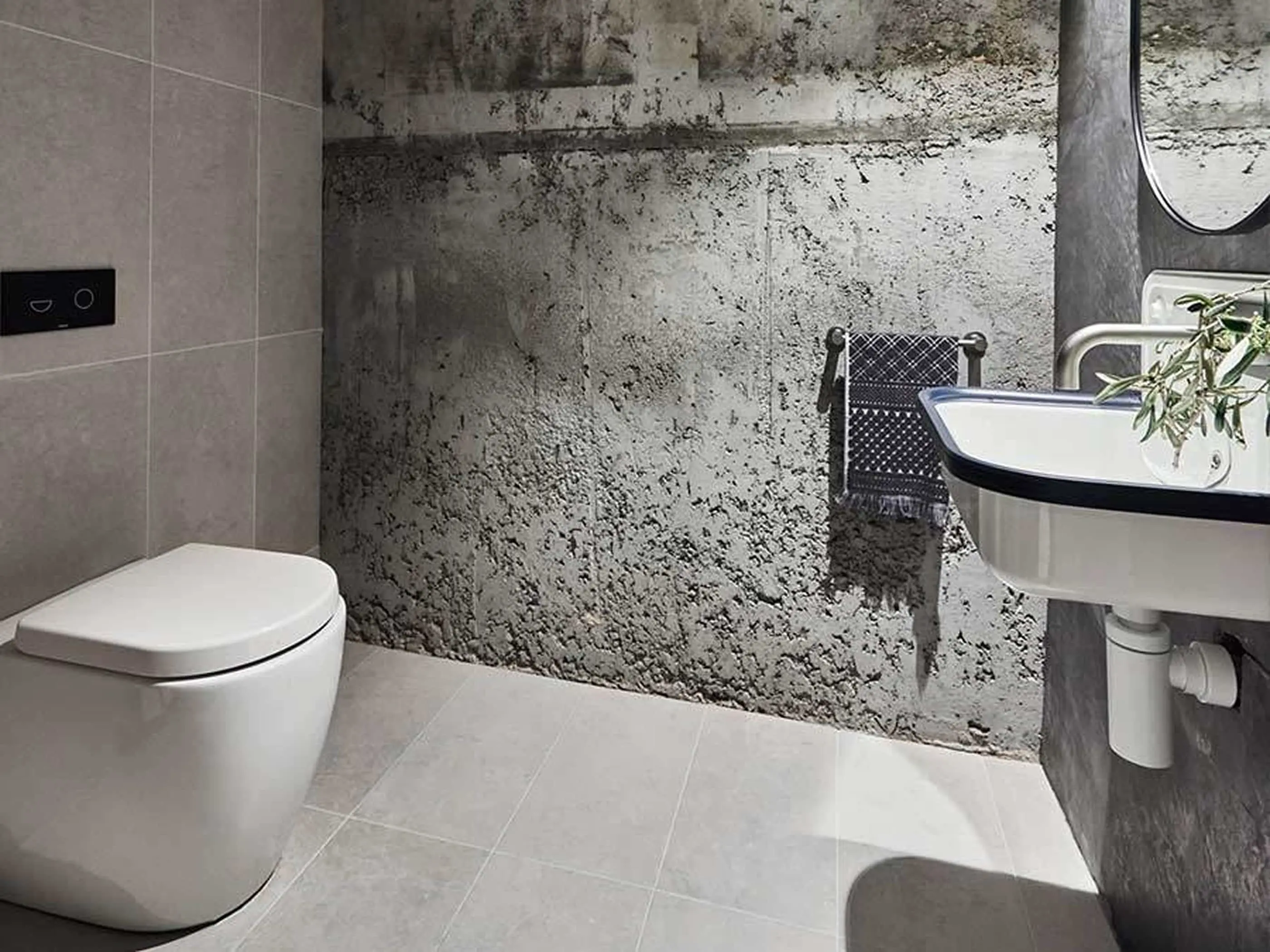 Modern bathroom with white toilet, wall-mounted sink, textured concrete wall, and small plant in a minimalist design.