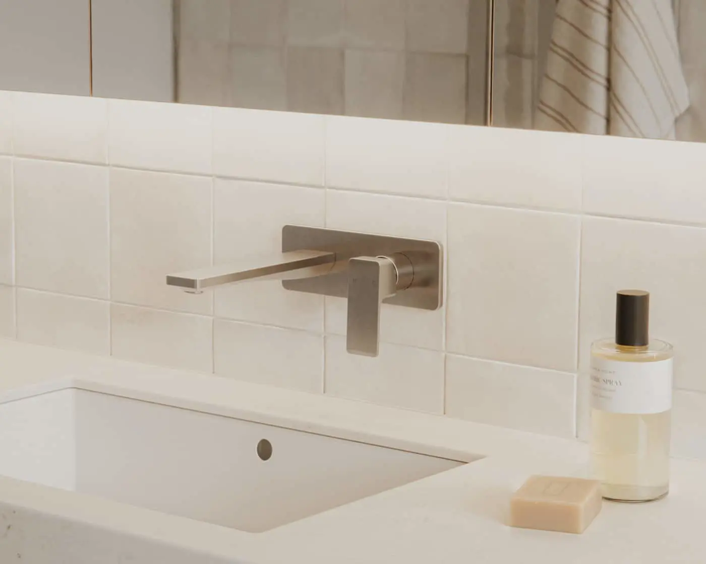 Modern bathroom sink with wall-mounted brushed nickel faucet, white tile backsplash, and toiletry items on the counter.