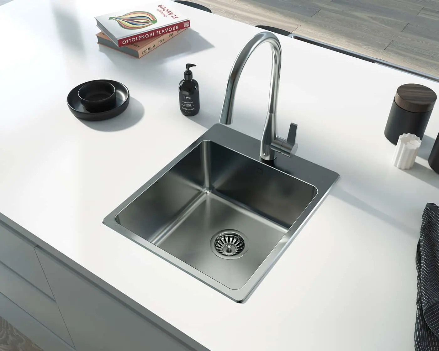 Modern stainless steel kitchen sink with arched faucet, soap dispenser, cookbooks, and black accessories on white countertop.